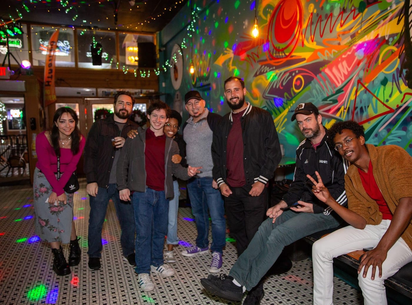 A group of Joybreak friends posing together in front of a colorful mural at a social night in downtown Orlando